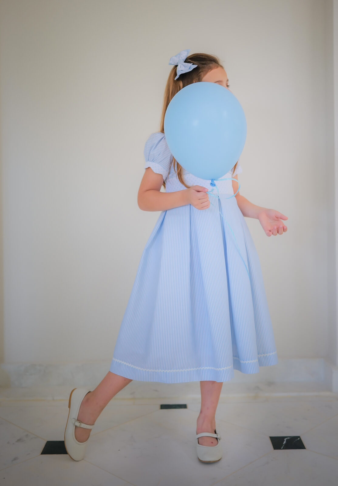Girl in a blue seersucker dress with a pale blue balloon