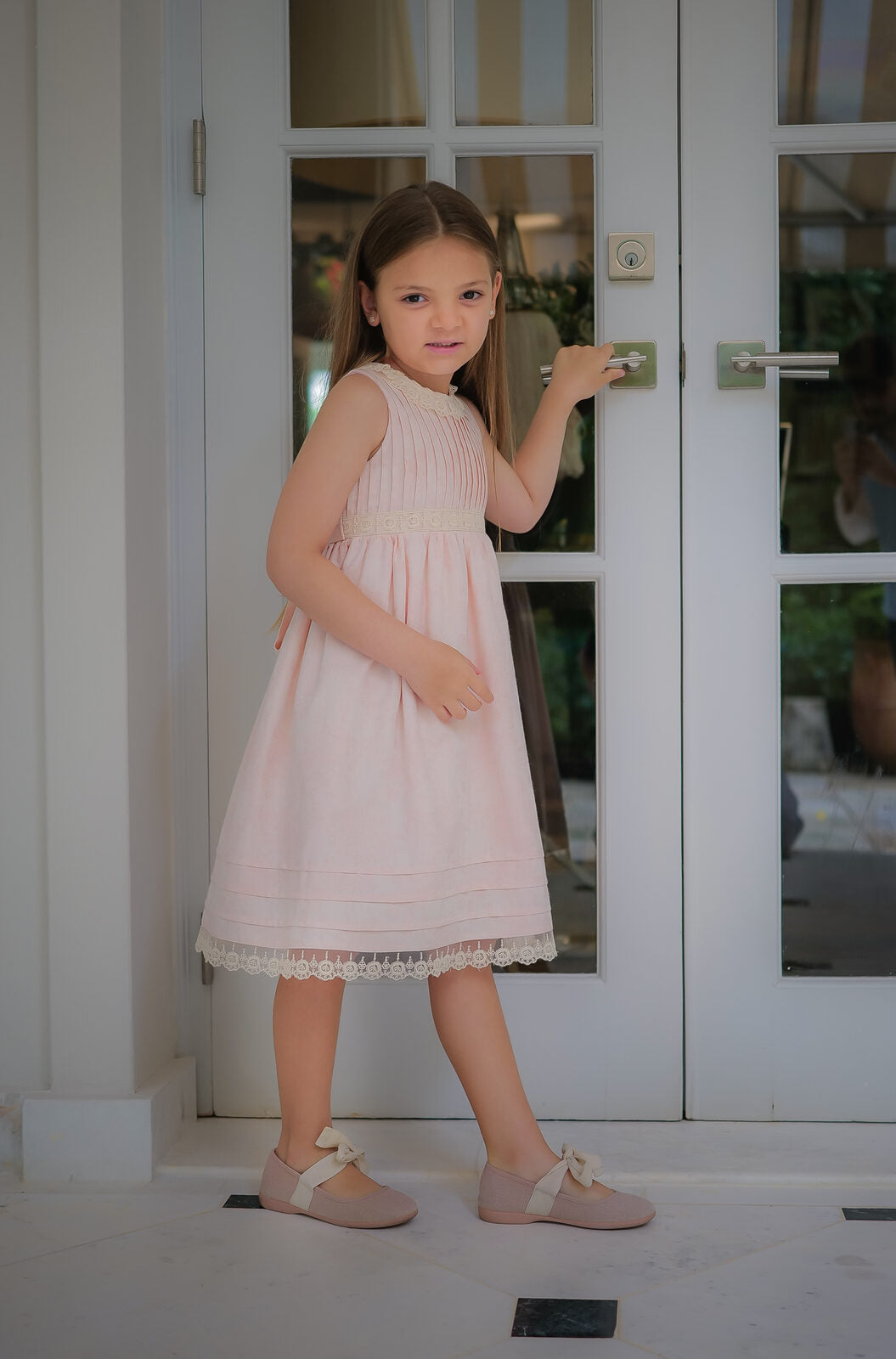 Girl in a pale pink pintuck dress with lace trim at white French doors