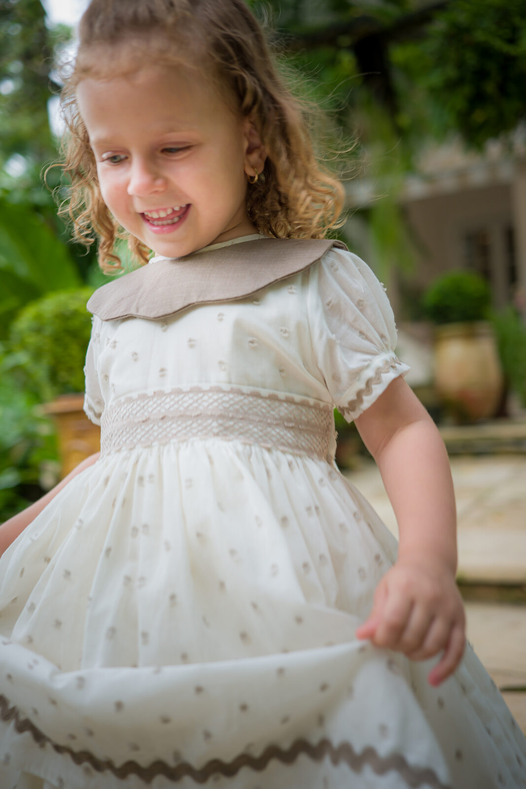 Girl twirling in an ivory smocked dress with a taupe collar