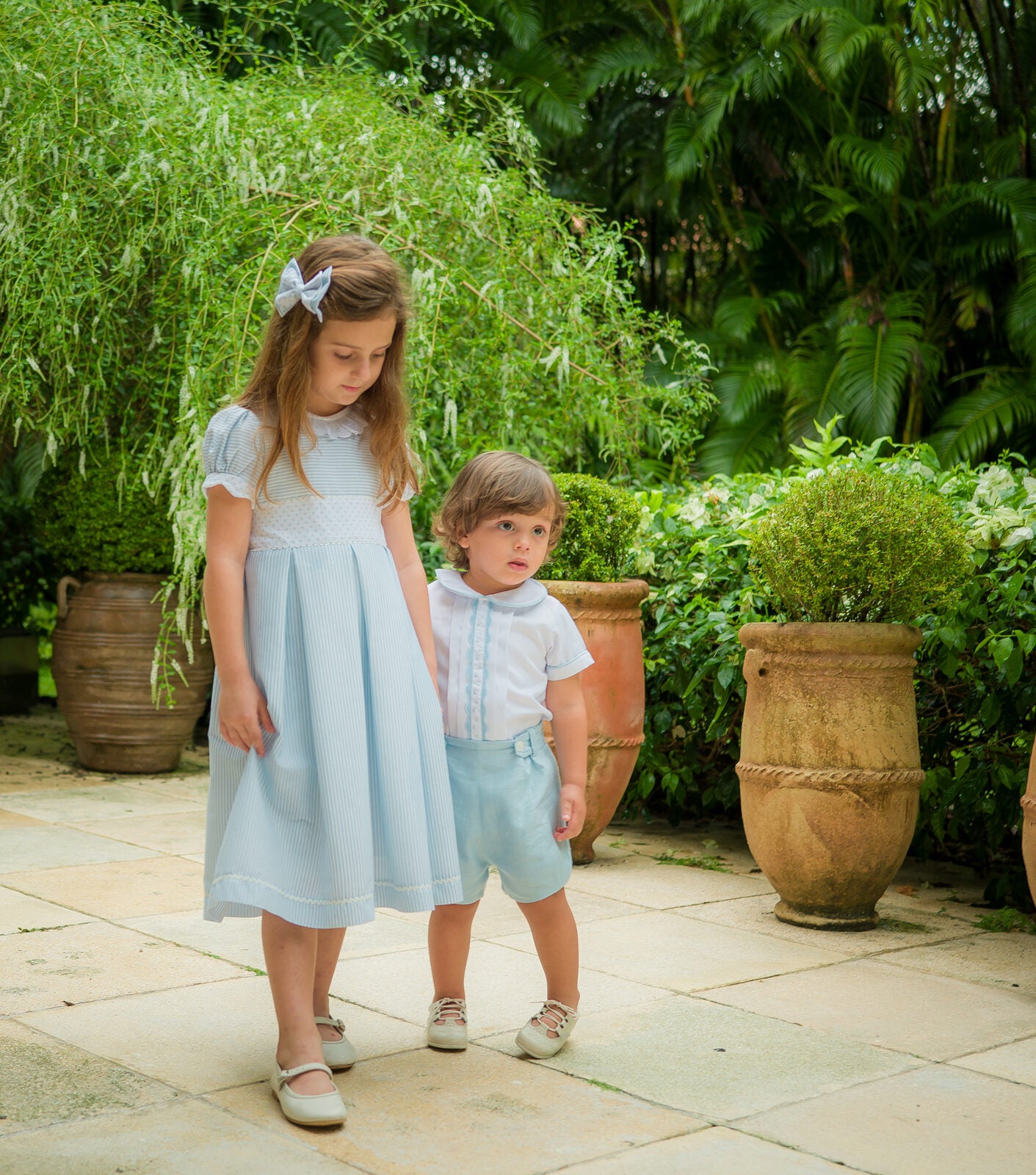 Girl in a blue striped dress beside a toddler in a white shirt and blue shorts